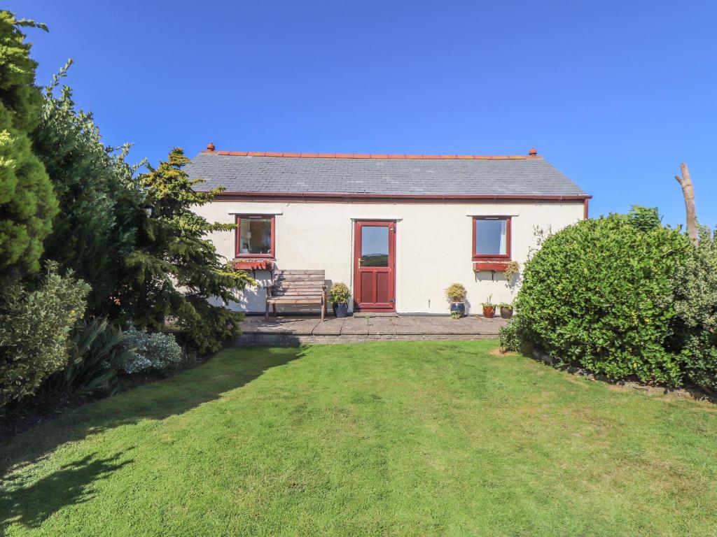 a white house with a red door and a yard at Bowling Green Cottage in Redruth