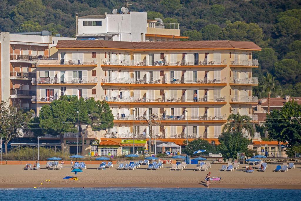 um grande edifício numa praia com cadeiras e pessoas em Hotel Rosa Nàutica em Malgrat de Mar