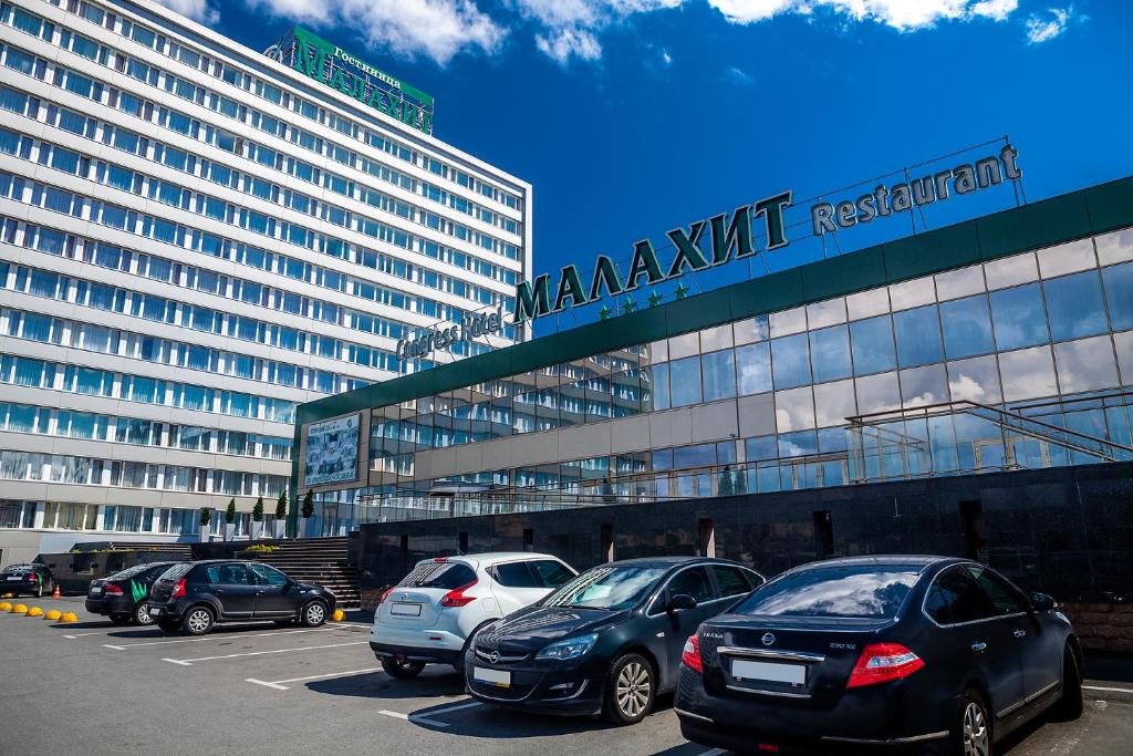 un aparcamiento con coches estacionados frente a un gran edificio en Congress Hotel Malakhit, en Chelyabinsk