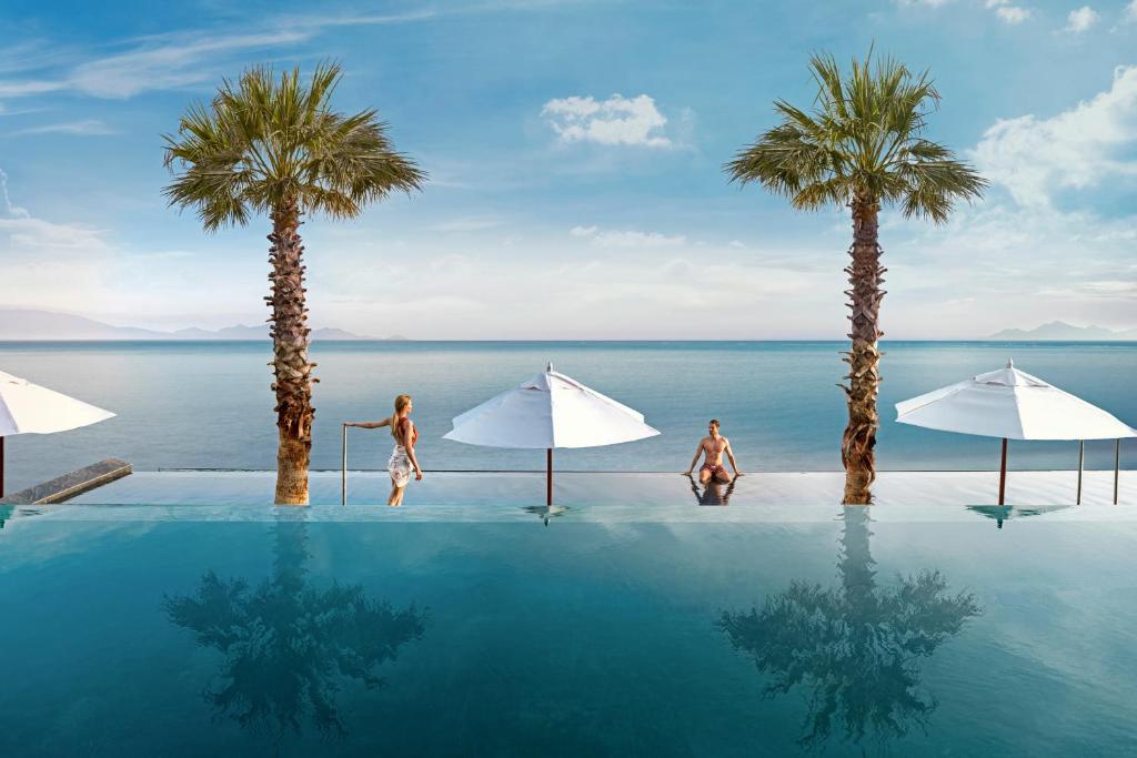 a swimming pool with two people and palm trees at Mitsis Summer Palace in Kardamaina