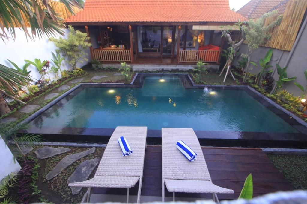 a swimming pool with two picnic tables in front of a house at Villa Rumah Lumbung The Wooden House in Ubud