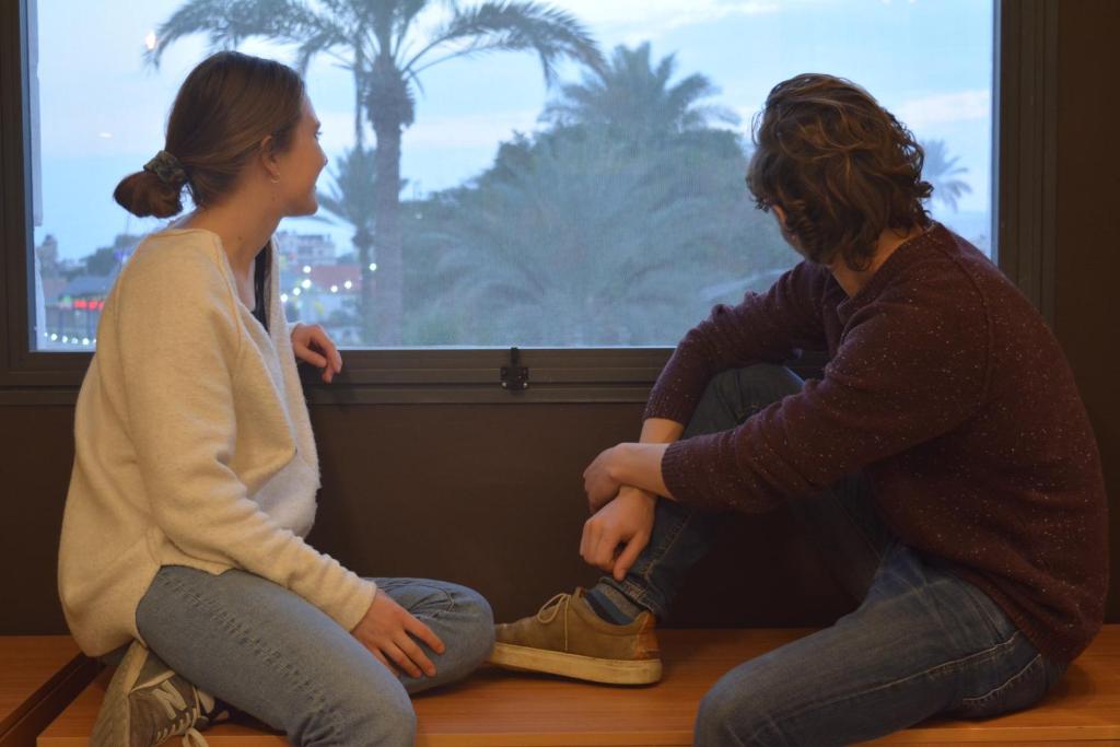 dwie kobiety siedzące na podłodze patrzące przez okno w obiekcie MOUNT41 Hostel w mieście Jerycho