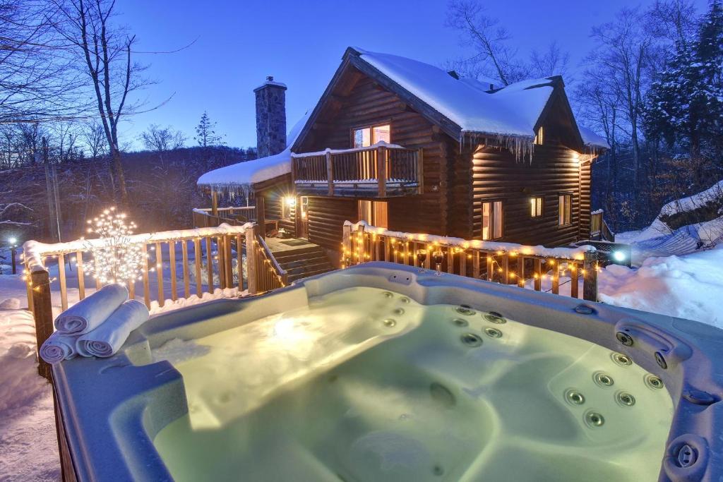 bañera de hidromasaje frente a una cabaña de madera en la nieve en Chic Familiale, Relaxant avec spa en montagnes en Labelle