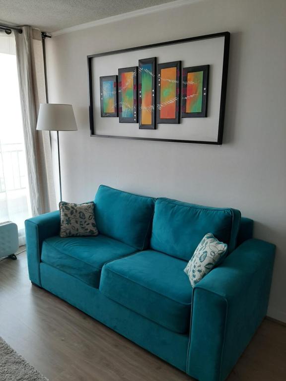 a blue couch in a living room with paintings on the wall at departamento santiago centro frente club hipico y movistar arena in Santiago