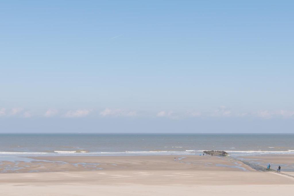 a beach with people walking on the sand and the ocean at Charmant appartement met frontaal zeezicht in Middelkerke