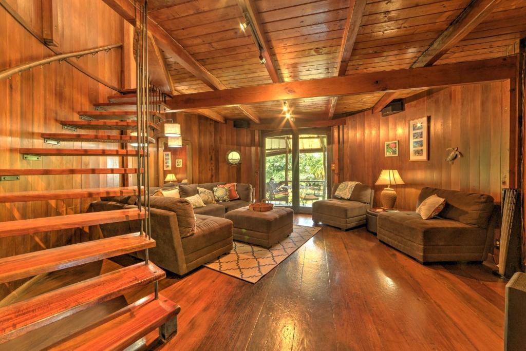 a living room with wooden walls and a spiral staircase at Tropical Cabana with Deck, Hot Tub and Lush Scenery! in Keaau