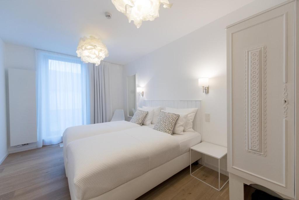 a white bedroom with a white bed and a chandelier at Berdorfer Eck - Bed&Breakfast in Berdorf