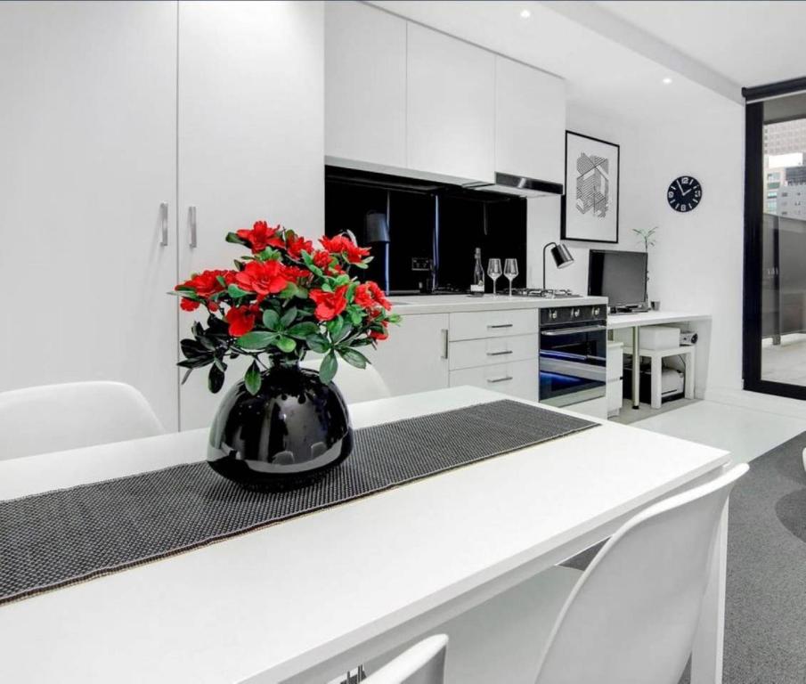 a white kitchen with a vase with red flowers on a counter at ReadySet Apartments on Little Collins in Melbourne