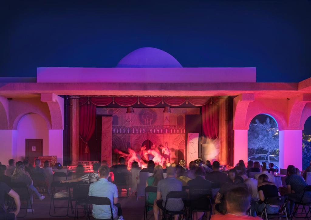 a crowd of people sitting in front of a stage with a fire at Mitsis Selection Blue Domes in Kardamaina