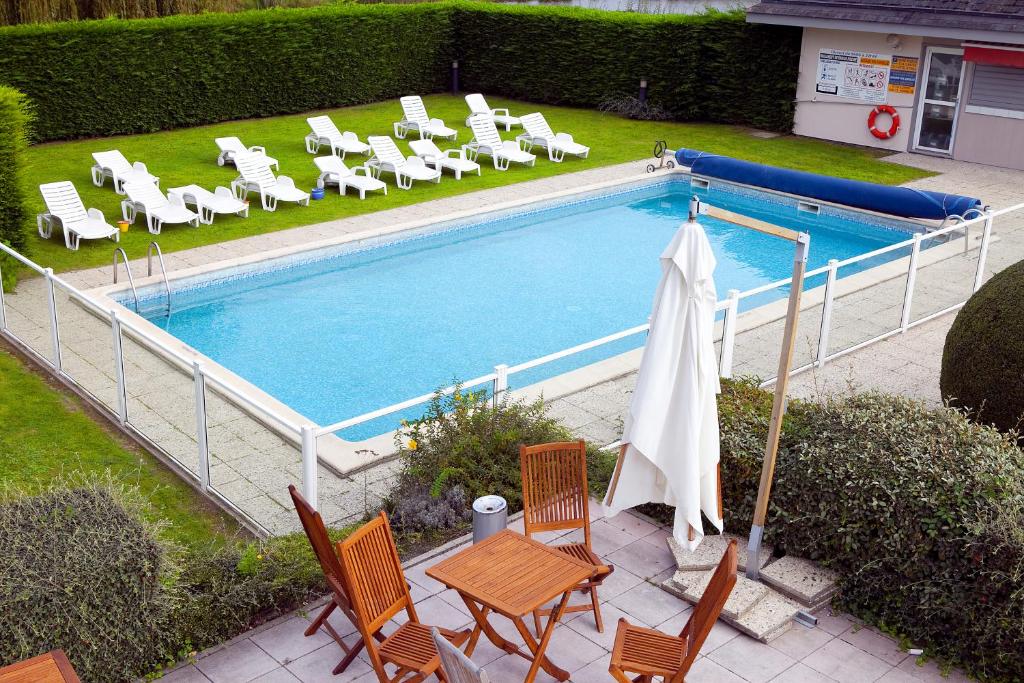 een uitzicht op een zwembad met stoelen en een parasol bij Kyriad Deauville - St Arnoult in Deauville