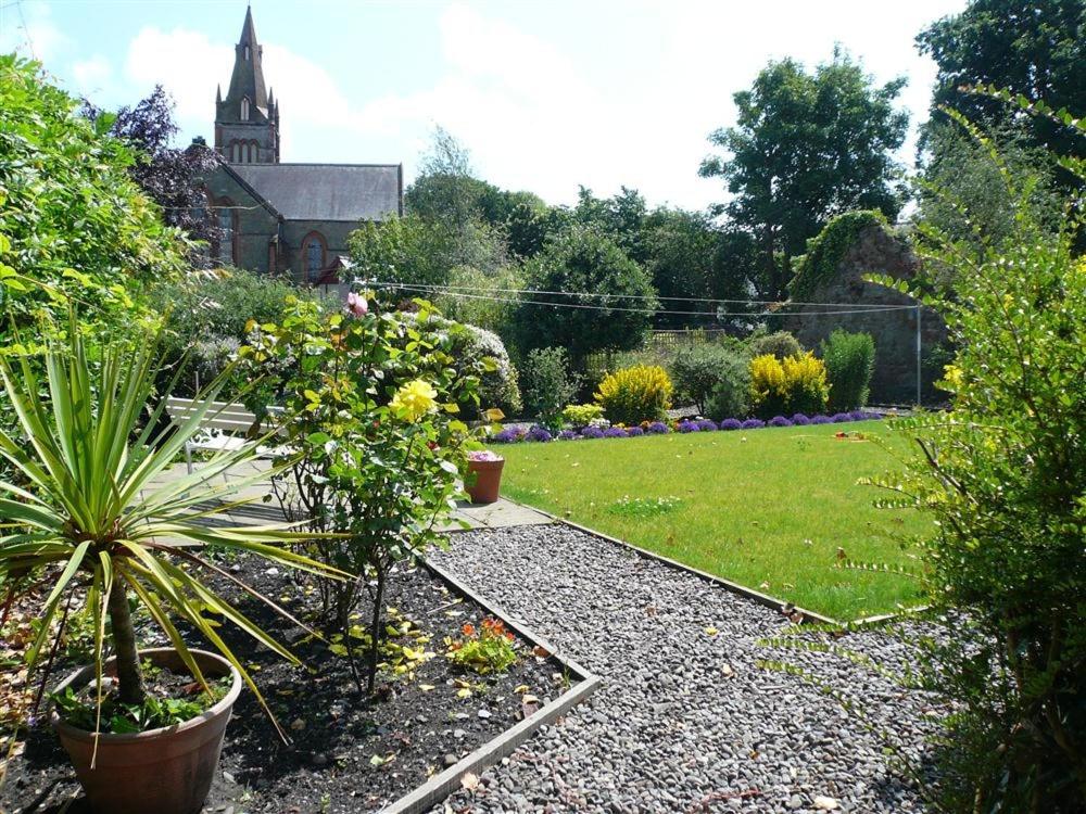 a garden with plants and a church in the background at Mackenzie House in Kirkcudbright