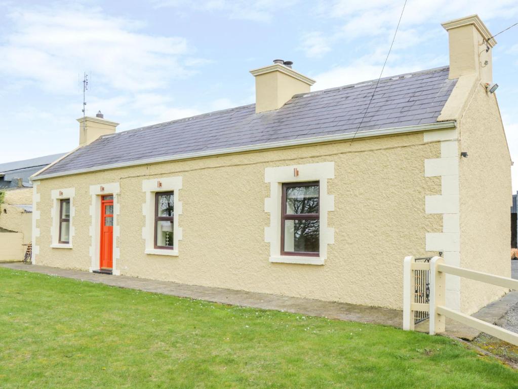 uma casa de tijolos amarelos com uma porta vermelha em Glor Cottage em Ballyhaunis