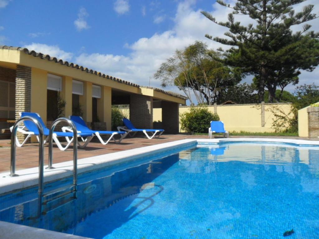 una piscina con sillas azules y una casa en Villas Aloha Valdelagrana, en El Puerto de Santa María