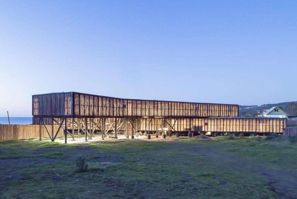 a wooden building in a field next to the ocean at Hotel Punta Sirena in Curanipe