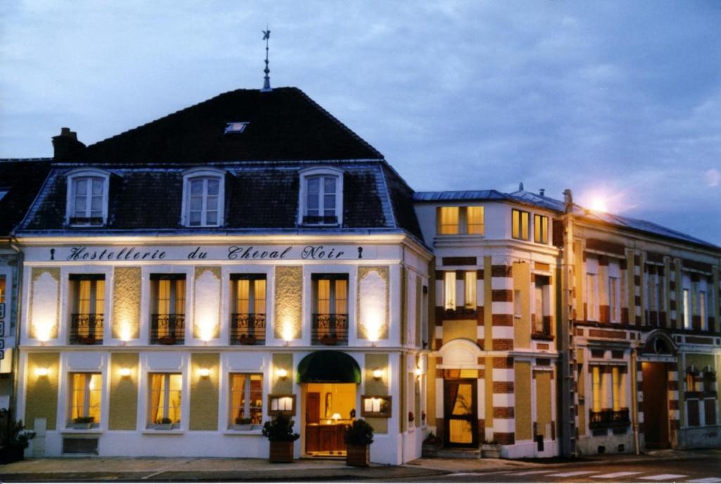 un grand bâtiment blanc avec un toit noir dans l'établissement L'Hôtel Le Cheval Noir, à Moret-sur-Loing