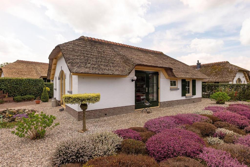une petite maison blanche avec des fleurs violettes dans la cour dans l'établissement Vakantiebungalow De Heivliet op de Veluwe, à Putten