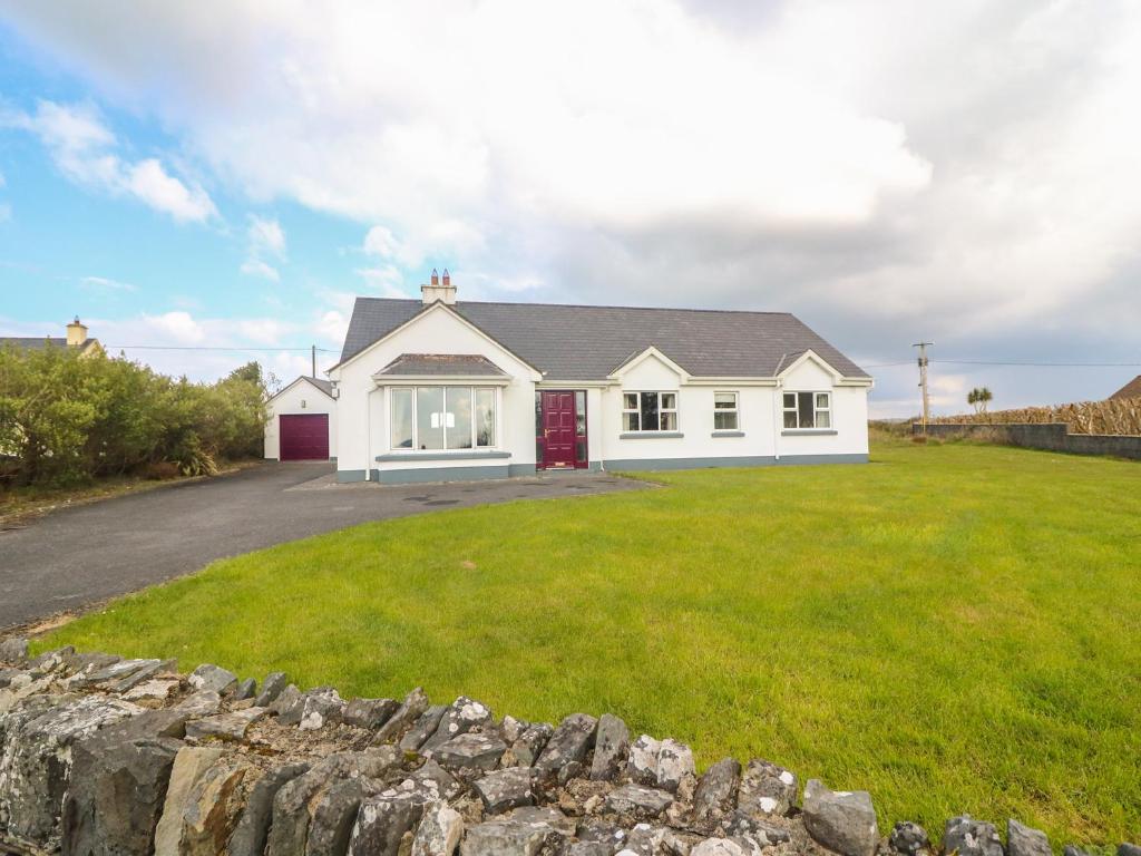 a white house with a stone wall in front of a yard at Cleary Cottage in Milltown Malbay