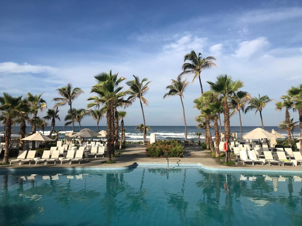 una piscina en la playa con palmeras y sillas en Villa dentro del Hotel Vidanta Mayan Palace en Acapulco