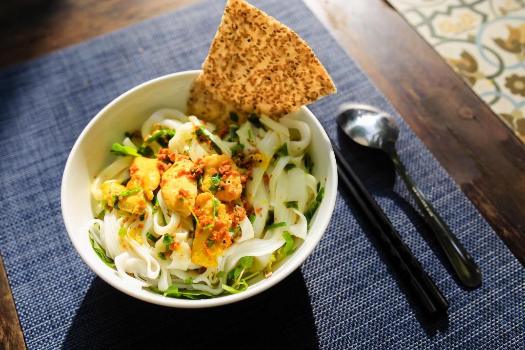 A bowl of rice noodles with herbs and a crisp bread accompaniment.