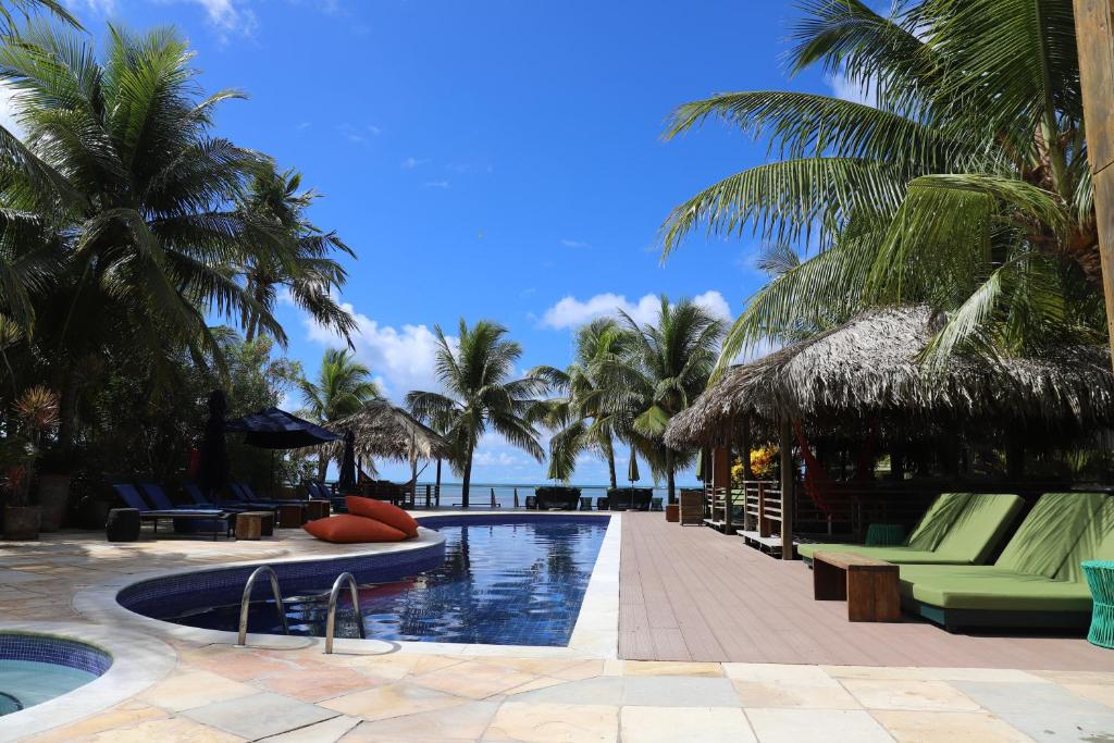 uma piscina de resort com palmeiras e o oceano em Pousada do Toque em São Miguel dos Milagres