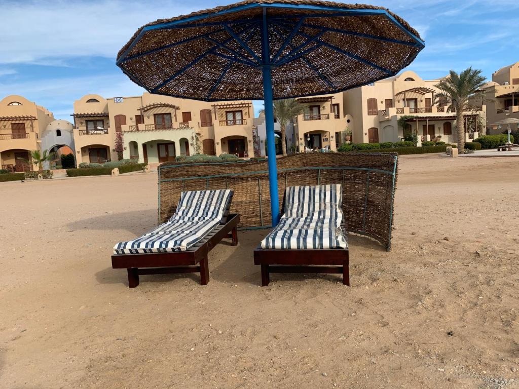 two benches sitting under an umbrella on the beach at One-Bedroom apartment ground floor for Rent in El Gouna in Hurghada