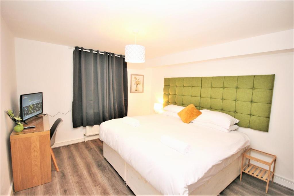 a bedroom with a large white bed with a green headboard at The Aldgate Rooms in London