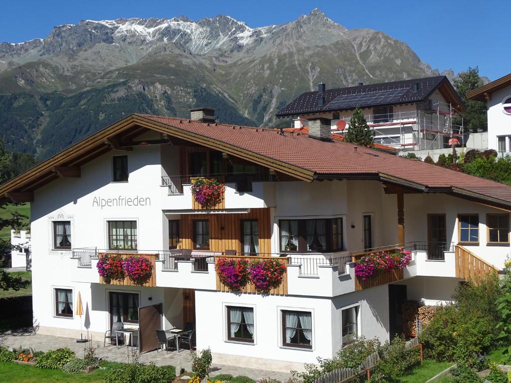 ein weißes Apartmenthaus mit Blumen vor den Bergen in der Unterkunft Alpenfrieden - Nauders in Nauders