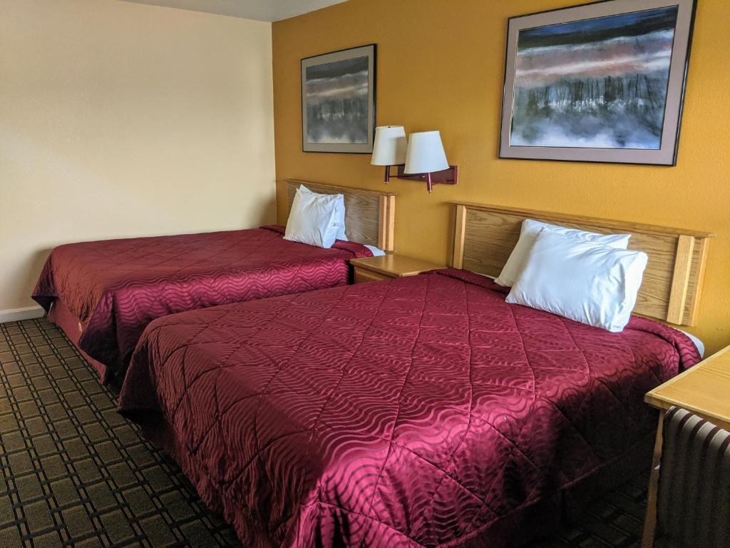 two beds in a hotel room with red sheets at Executive Inn in Fort Wayne