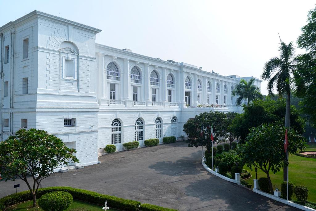 a large white building with a courtyard and palm trees at Maidens Hotel New Delhi in New Delhi