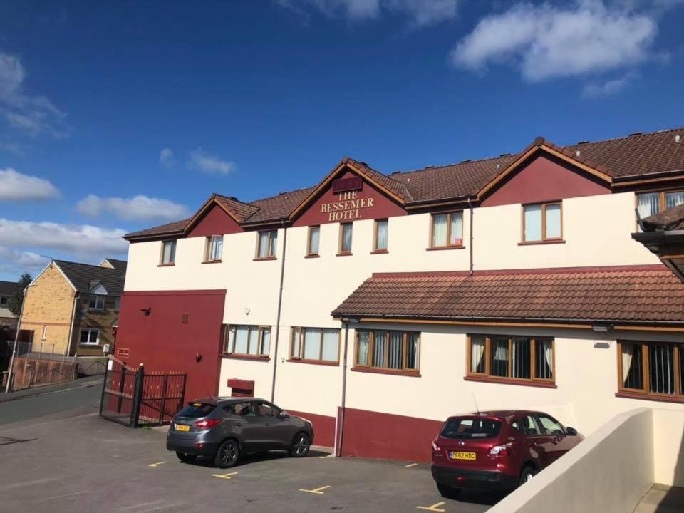 dos autos estacionados en un estacionamiento frente a un edificio en Bessemer Hotel, en Merthyr Tydfil