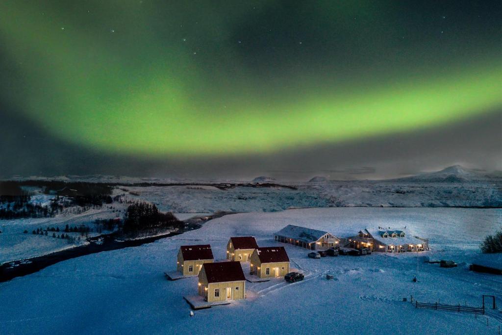 una aurora sobre un grupo de casas en la nieve en Hótel Lækur en Hella