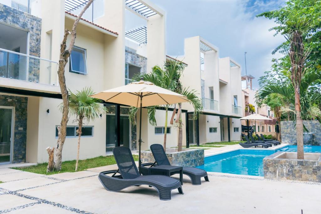 a villa with a swimming pool and two chairs and an umbrella at Increíble estudio en Puerto Aventuras, Condominio con alberca # 201 in Puerto Aventuras