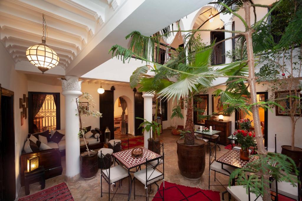 ein Wohnzimmer mit Tischen, Stühlen und Pflanzen in der Unterkunft Riad des trois palais in Marrakesch