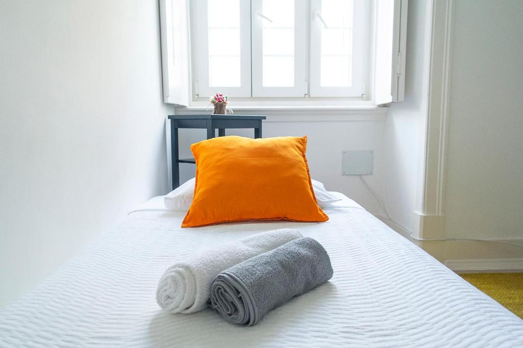 an orange pillow and two towels on a bed at Guest House Amoreiras in Lisbon