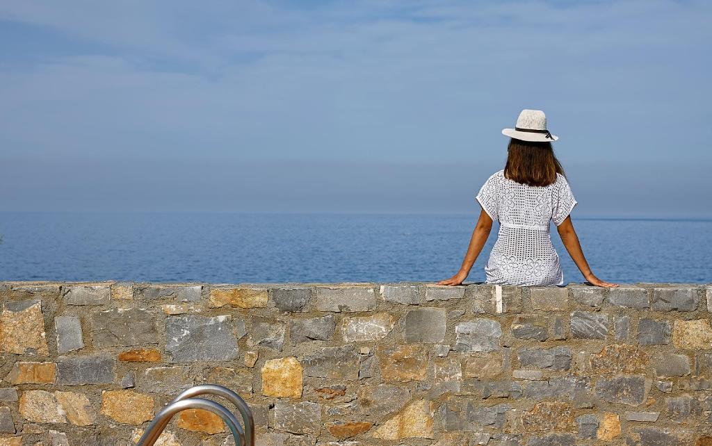 a woman sitting on a wall looking at the ocean at Vasia Resort & Spa in Sisi