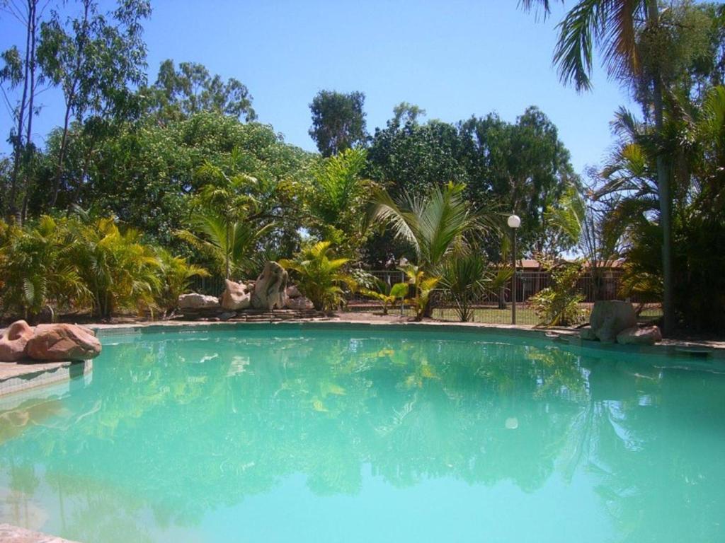 a large swimming pool with blue water and trees at Territory Manor Motel & Caravan Park in Mataranka