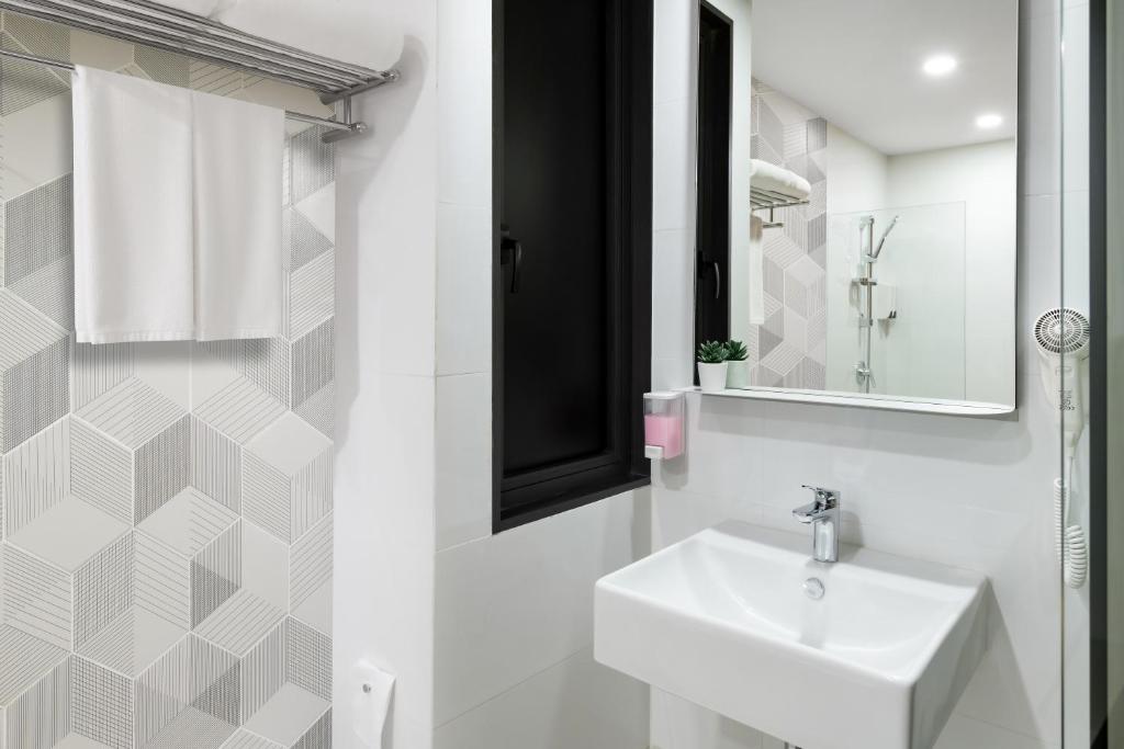 A bright bathroom shows a wall-mounted basin, large mirror and geometric tile accent wall.