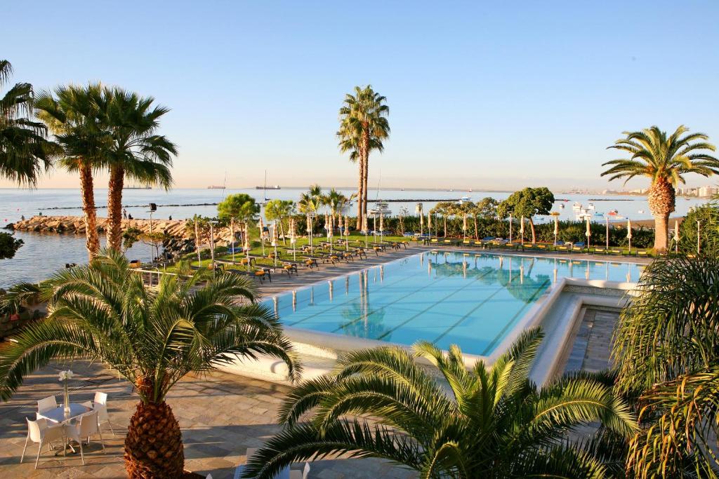 a pool with palm trees and chairs and the ocean at Crowne Plaza Limassol by IHG in Limassol