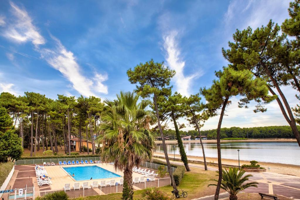 a resort swimming pool with a beach and trees at SOWELL Family Pignada Plage in Soustons