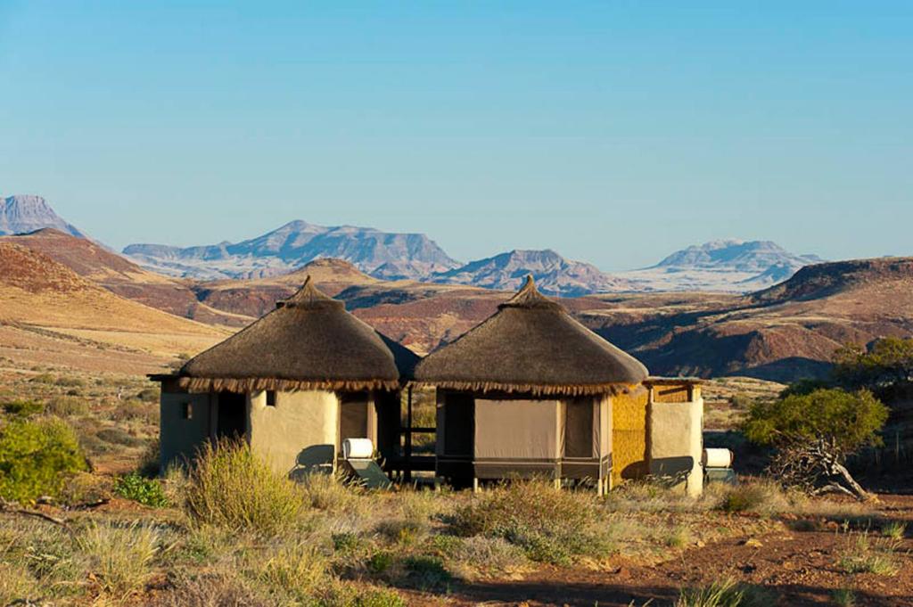 two huts in the desert with mountains in the background at Wilderness Safaris Damaraland Camp in Twyfelfontein