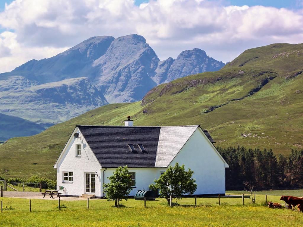 a white house in a field with mountains in the background at Holiday Home Strath Glebe by Interhome in Broadford