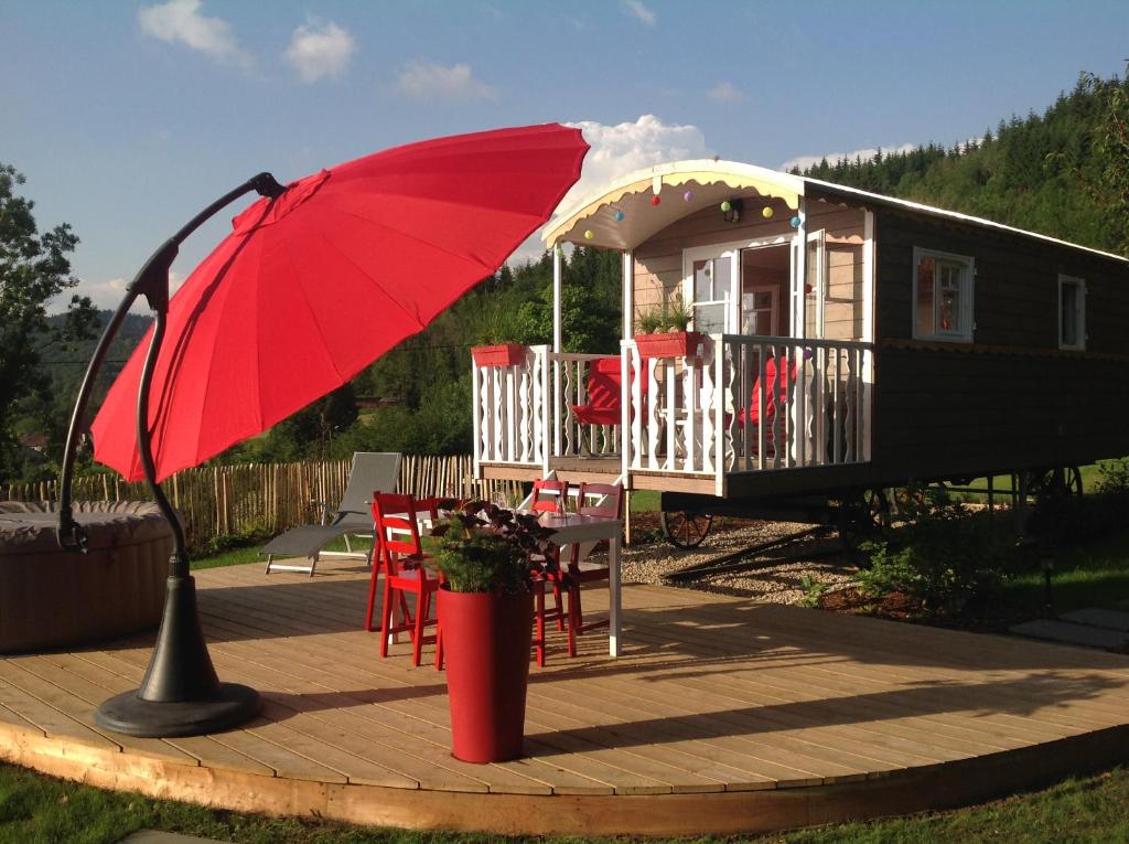 un parasol rouge assis sur une terrasse à côté d'une maison dans l'établissement la roulotte arc-en-ciel, à Villards-dʼHéria