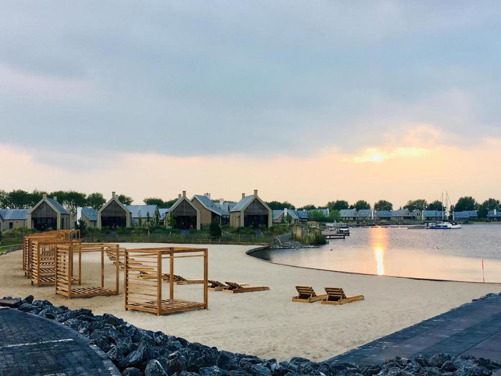 a sandy beach with benches and houses on the water at Holiday Home Oesterdam Resort by Interhome in Tholen