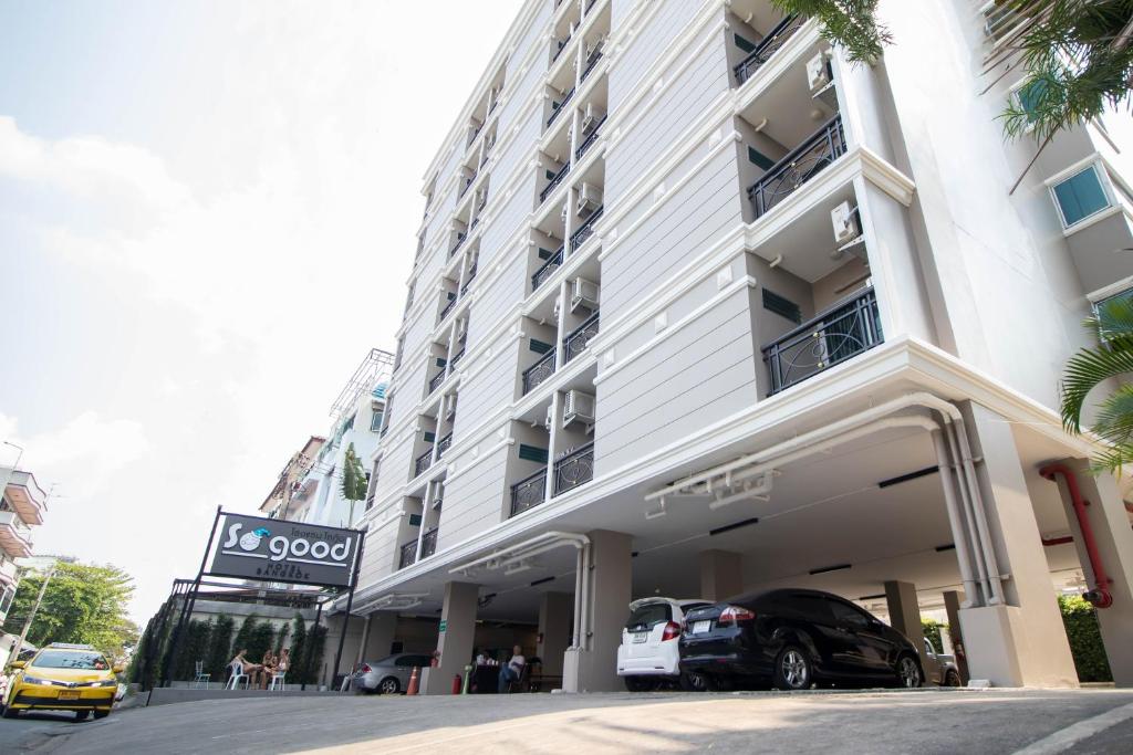 um grande edifício branco com carros estacionados em frente em So good Hotel Bangkok em Bangkok