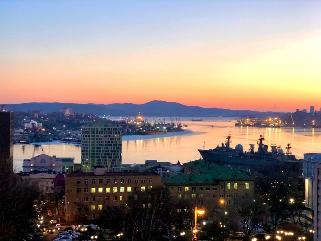 a view of a city at sunset with a ship in the water at Golden Bridge View Apt in Vladivostok