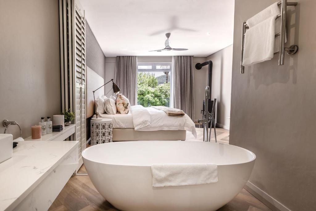 a white bath tub in a bathroom with a bed at Franschhoek Boutique Hotel - Lion Roars Hotels & Lodges in Franschhoek