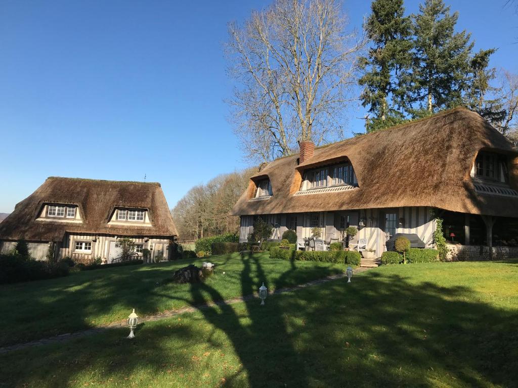 2 cottages au toit de chaume sur une pelouse verdoyante avec un arbre dans l'établissement Les chaumières du pays d'auge, à Le Breuil-en-Auge