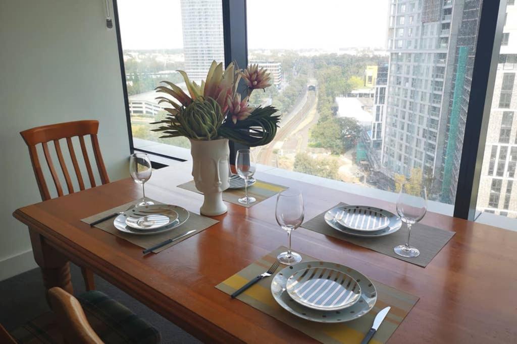 a wooden table with wine glasses and plates on it at Modern apartment+office w Parking @ Olympic Park in Sydney
