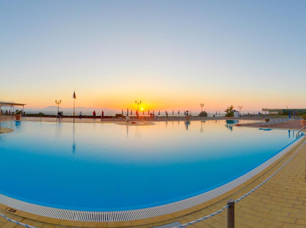 a large swimming pool with a sunset in the background at TH Cinisi - Florio Park Hotel in Cinisi
