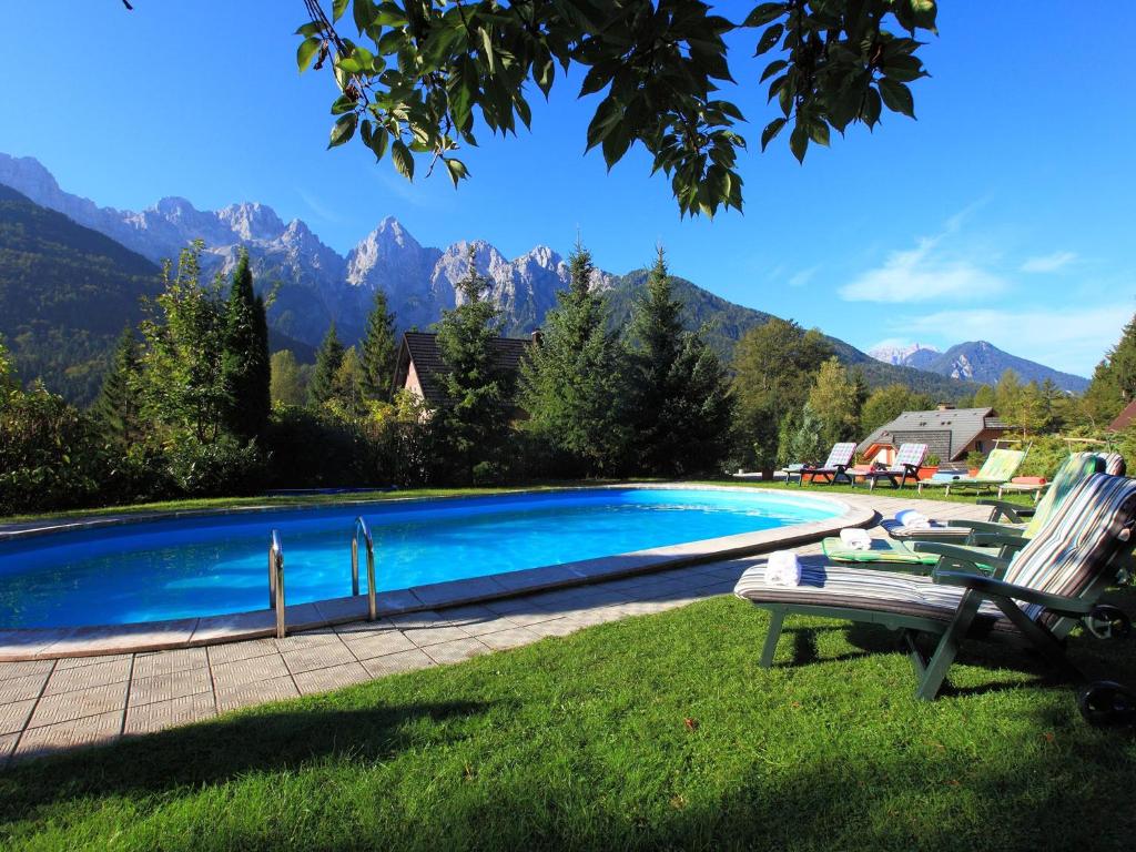 a swimming pool with chairs and mountains in the background at Vila Edelweiss Rooms&App Kranjska Gora in Kranjska Gora